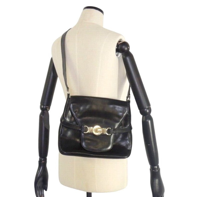 1970s Gucci saddle bag in black leather with muted gold hardware, an expandable bottom, wide shoulder strap, and burgundy leather lining