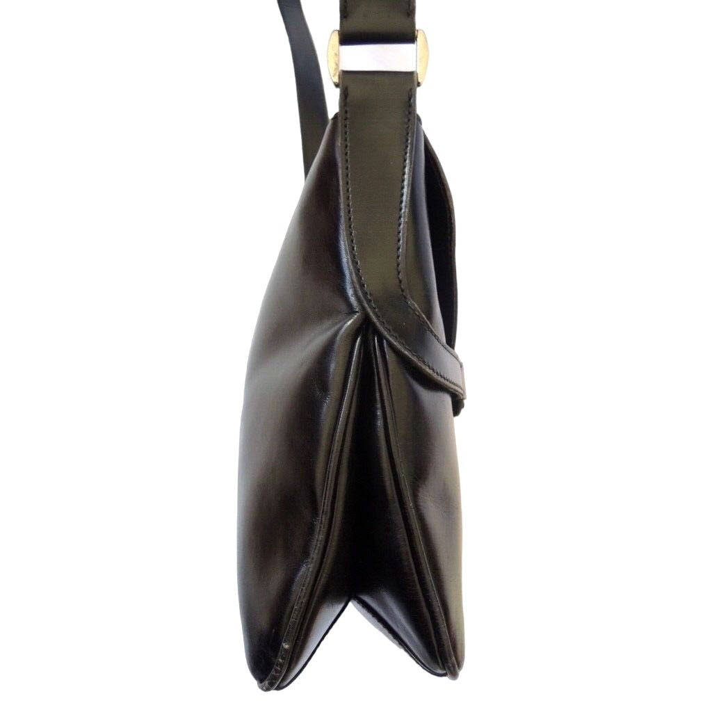 1970s Gucci saddle bag in black leather with muted gold hardware, an expandable bottom, wide shoulder strap, and burgundy leather lining
